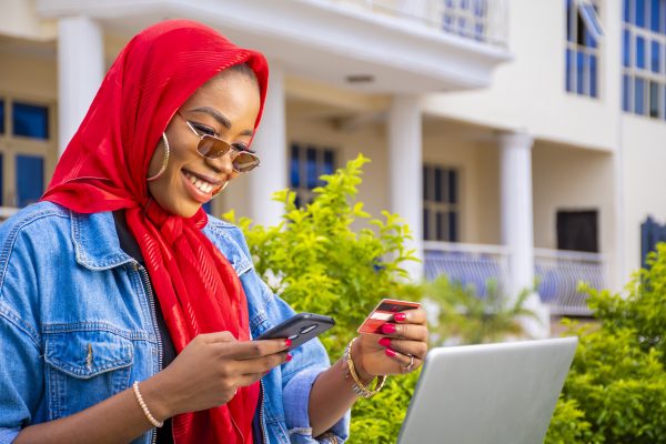 An African female happily shopping online using a laptop and a smartphone while holding her credit card